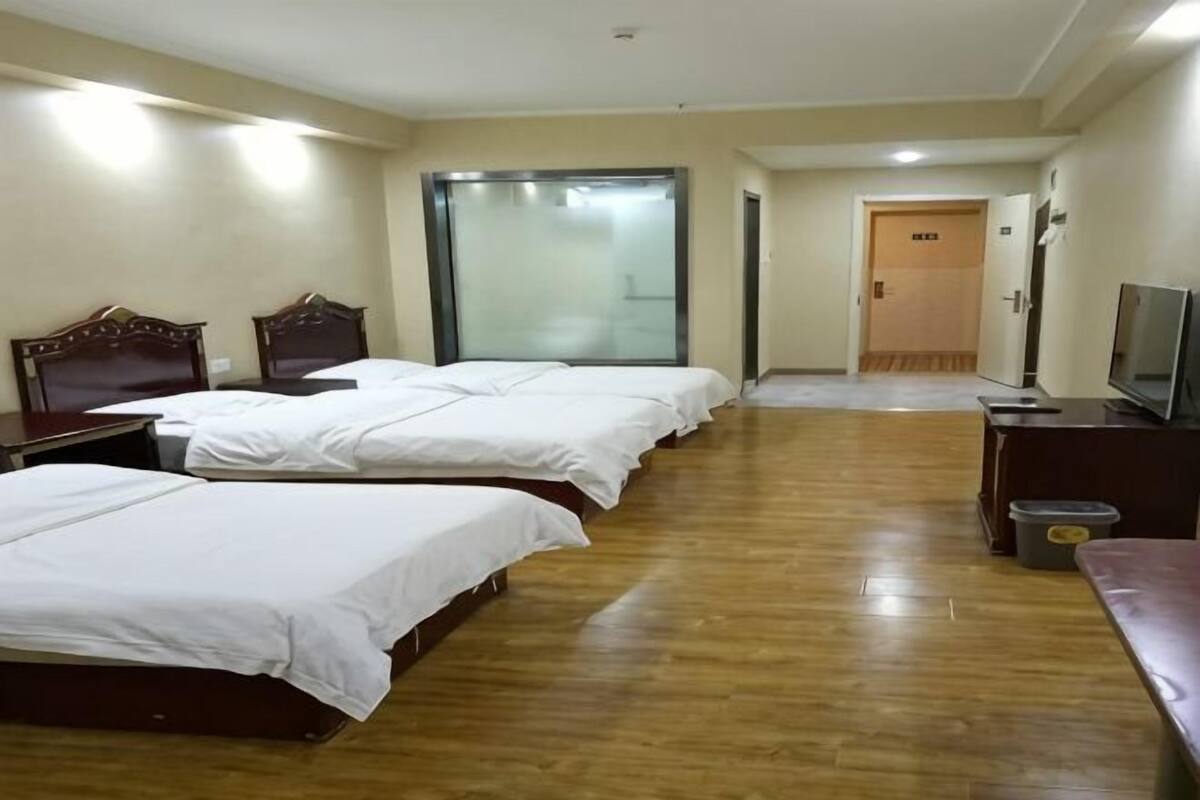 Ein Hotelzimmer mit vier Betten, einem Fernseher, einem Schreibtisch und einer Mülleimer.