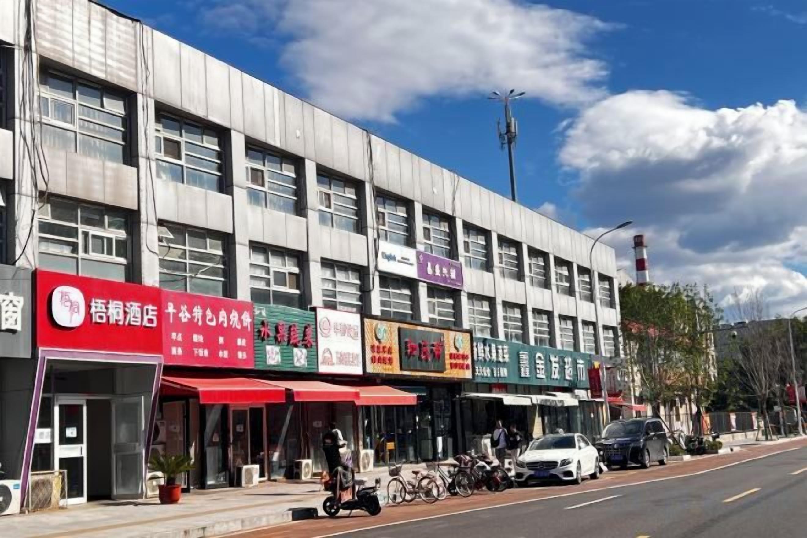 A row of commercial buildings with storefronts, a clear sky, and a street with parked vehicles.