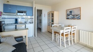 A compact kitchen with blue cabinets, a microwave, and a dining area with a table and chairs. - Apartment for 6, ocean view, Mimizan Beach, parking (Mimizan-Mimizan Plage)