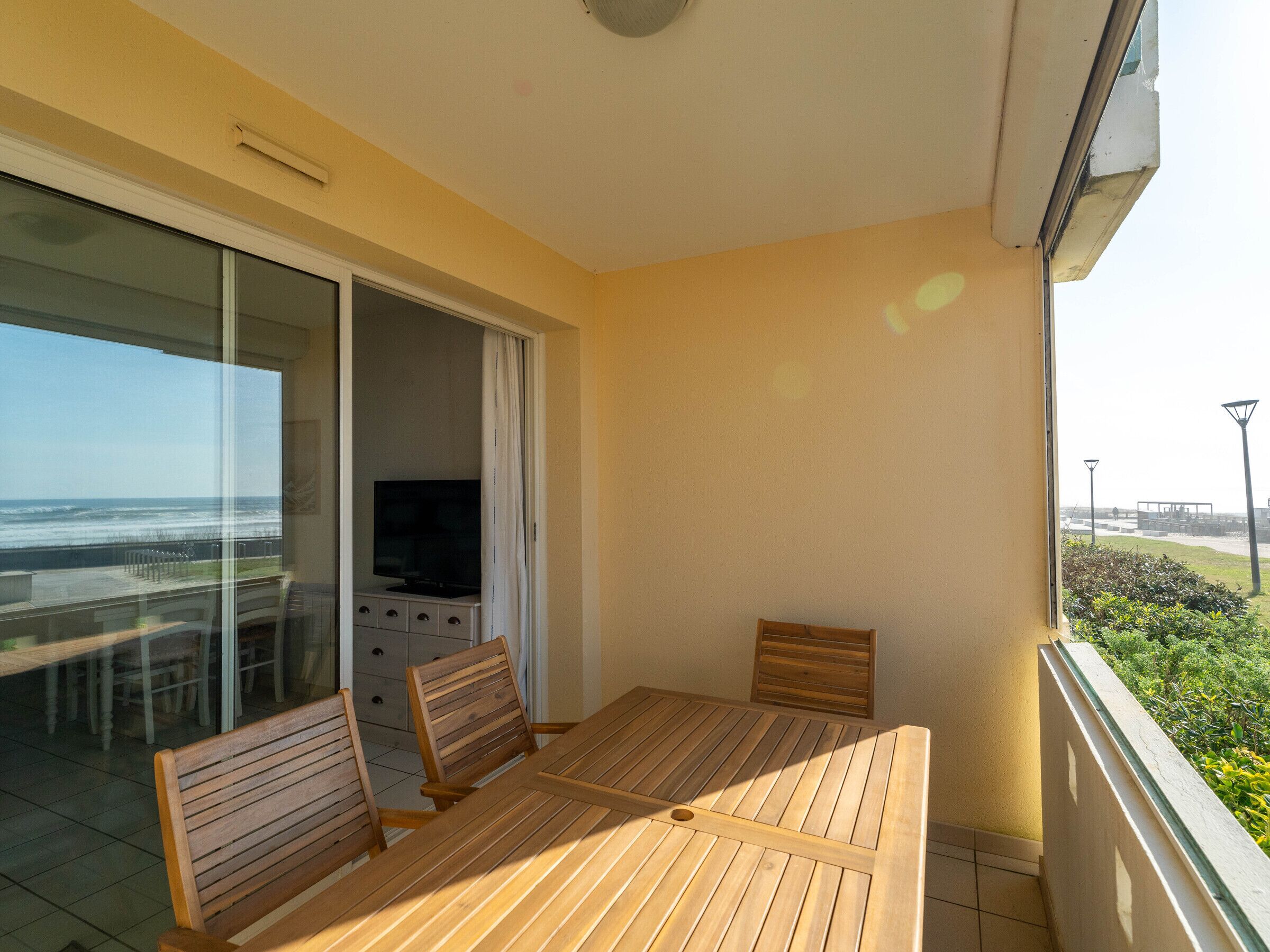 A balcony with a wooden table and chairs, a TV, and a view of the ocean.