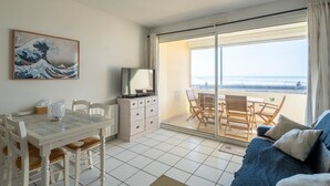 A room with a dining table, chairs, a TV, a sofa, and a balcony with a view of the ocean. - Apartment for 6, ocean view, Mimizan Beach, parking (Mimizan-Mimizan Plage)