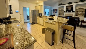 A spacious kitchen with granite countertops, a stainless steel refrigerator, and a dining area with a bar stool. - Entire Home Augusta, Martinez GA with Swimming pool (Martinez)