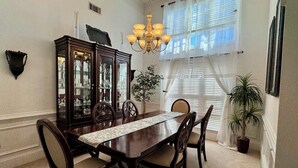 A dining area with a wooden table, six chairs, a chandelier, a cabinet with glass doors, and a potted plant. - Entire Home Augusta, Martinez GA with Swimming pool (Martinez)
