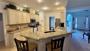 A modern kitchen with granite countertops, white cabinetry, and a central island with bar stools. - Entire Home Augusta, Martinez GA with Swimming pool (Martinez)