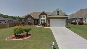 A two-story house with a garage, a well-maintained lawn, and a small garden area. - Entire Home Augusta, Martinez GA with Swimming pool (Martinez)