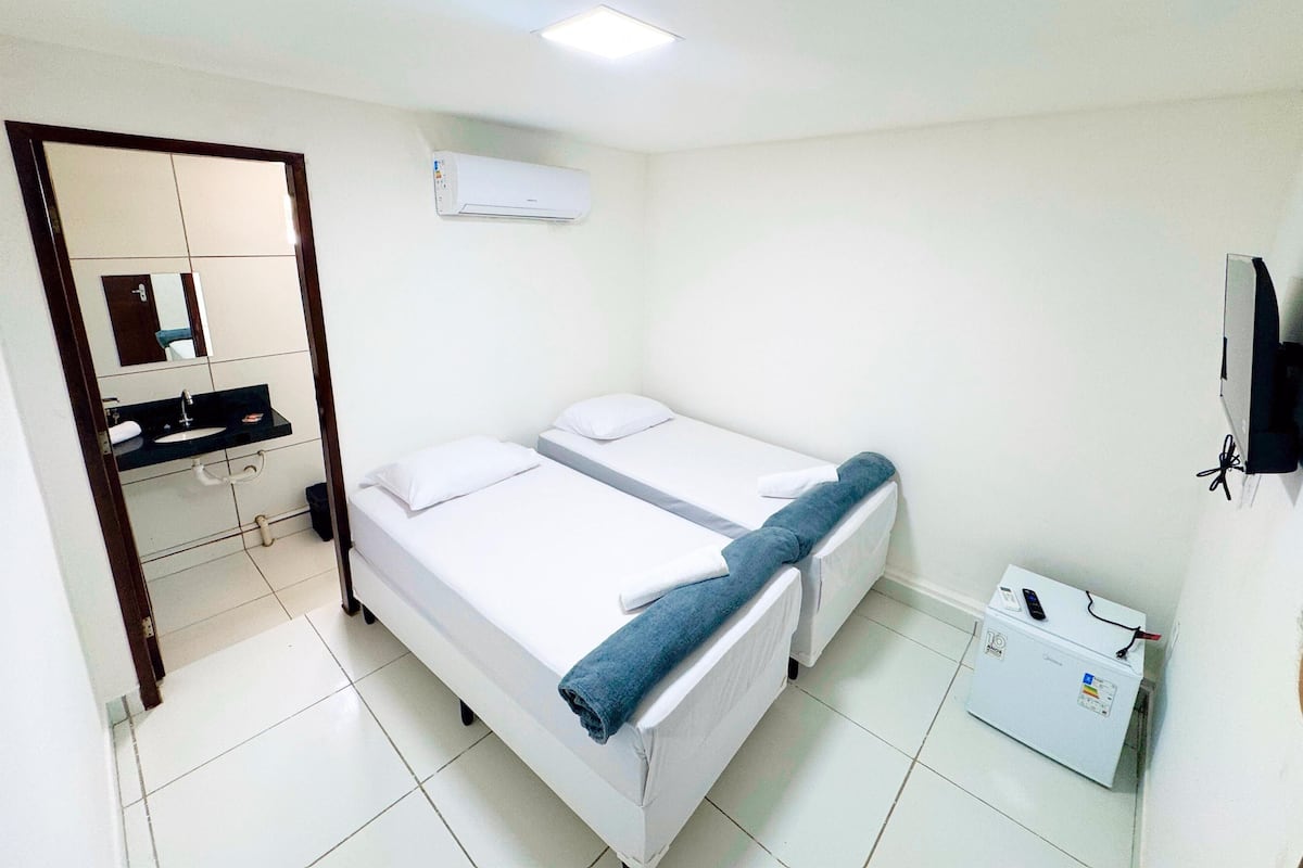 A small, clean room with a bed, a bathroom with a sink and mirror, and a TV on the wall.