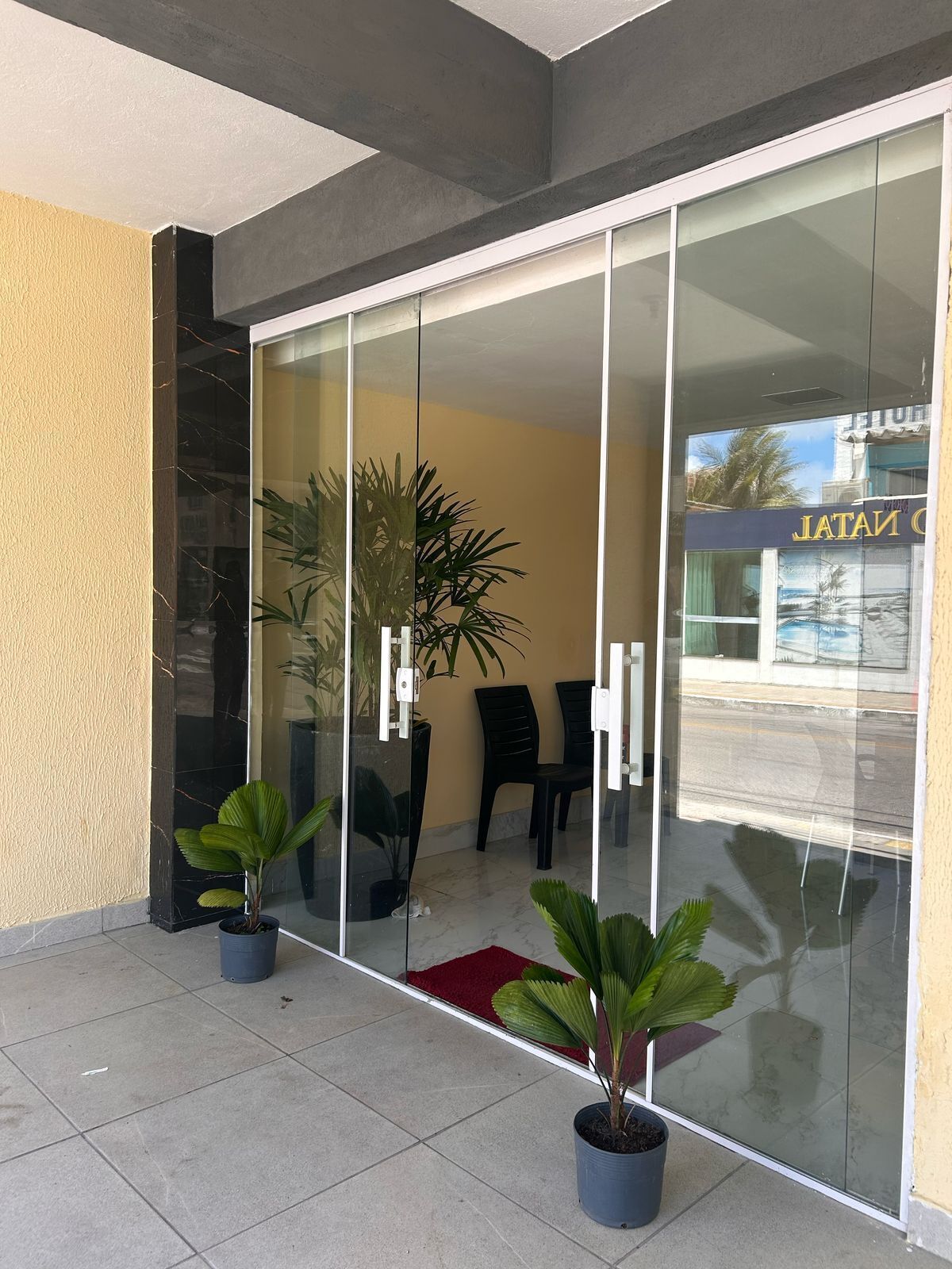 Entrada moderna de un edificio con puertas de vidrio, plantas en macetas y un letrero que dice 'JATAI'.