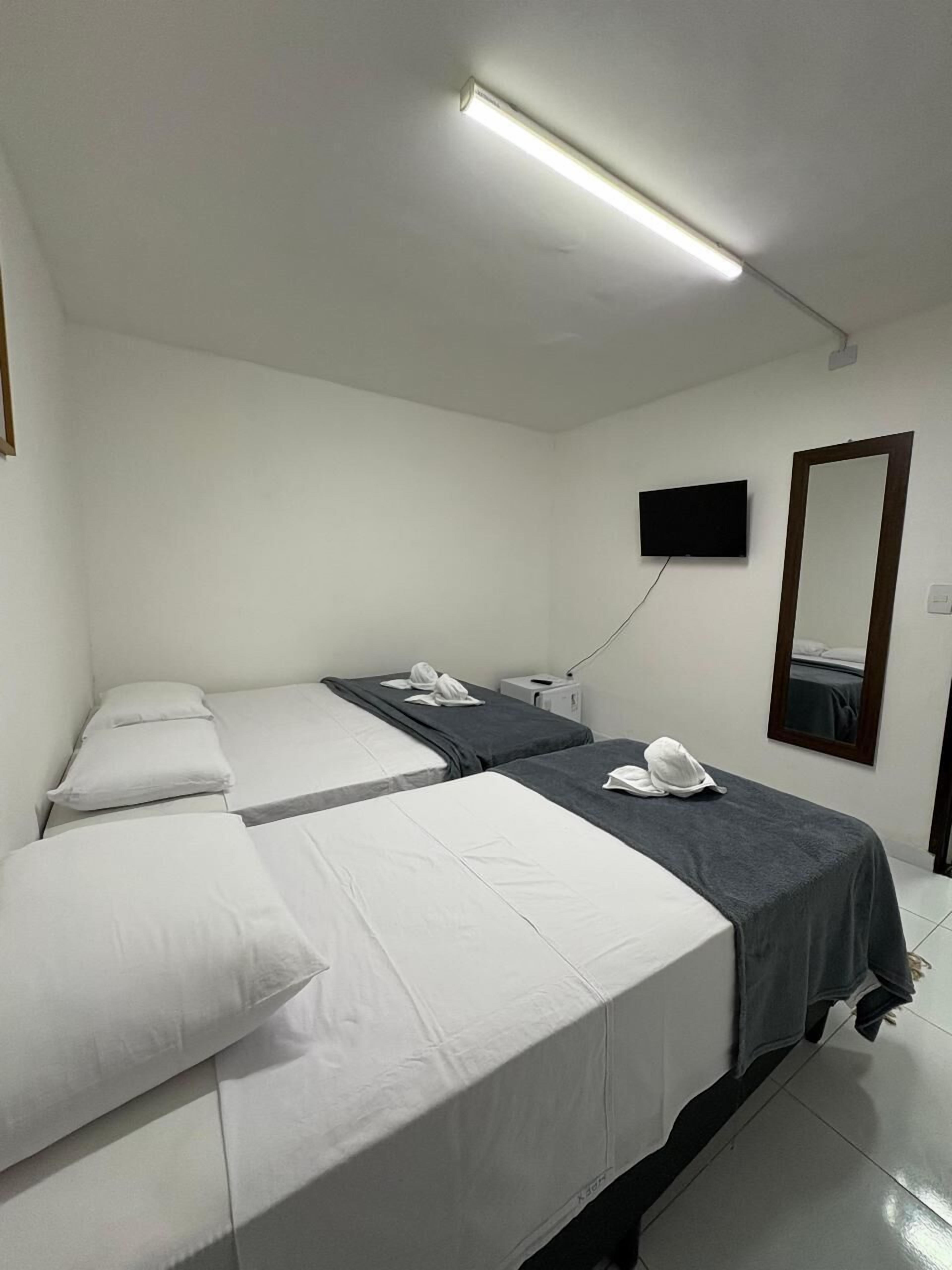 Habitació d'hotel amb dos llits individuals, un televisor de pantalla plana, un mirall i una làmpada al sostre.