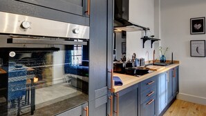 A modern kitchen with a built-in oven, stainless steel appliances, and a wooden countertop. - Homebird Property - The Vicarage (Leeds)