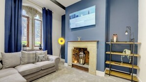 A living room with a sofa, a fireplace, a wall-mounted TV, and a bookshelf. - Homebird Property - The Vicarage (Leeds)