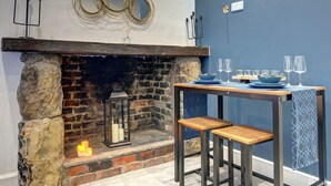 A stone fireplace with a wooden mantel, a table with blue plates and glasses, and a blue wall. - Homebird Property - The Vicarage (Leeds)