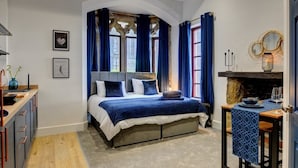 A bedroom with a large bed, a fireplace, and a dining area with a table and chairs. - Homebird Property - The Vicarage (Leeds)