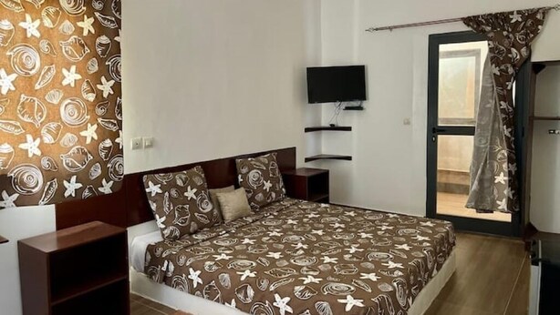 A bedroom with a bed, a TV, a small table, and a window with curtains.