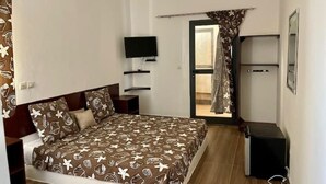 A bedroom with a bed, a TV, a wardrobe, and a door leading to a balcony.