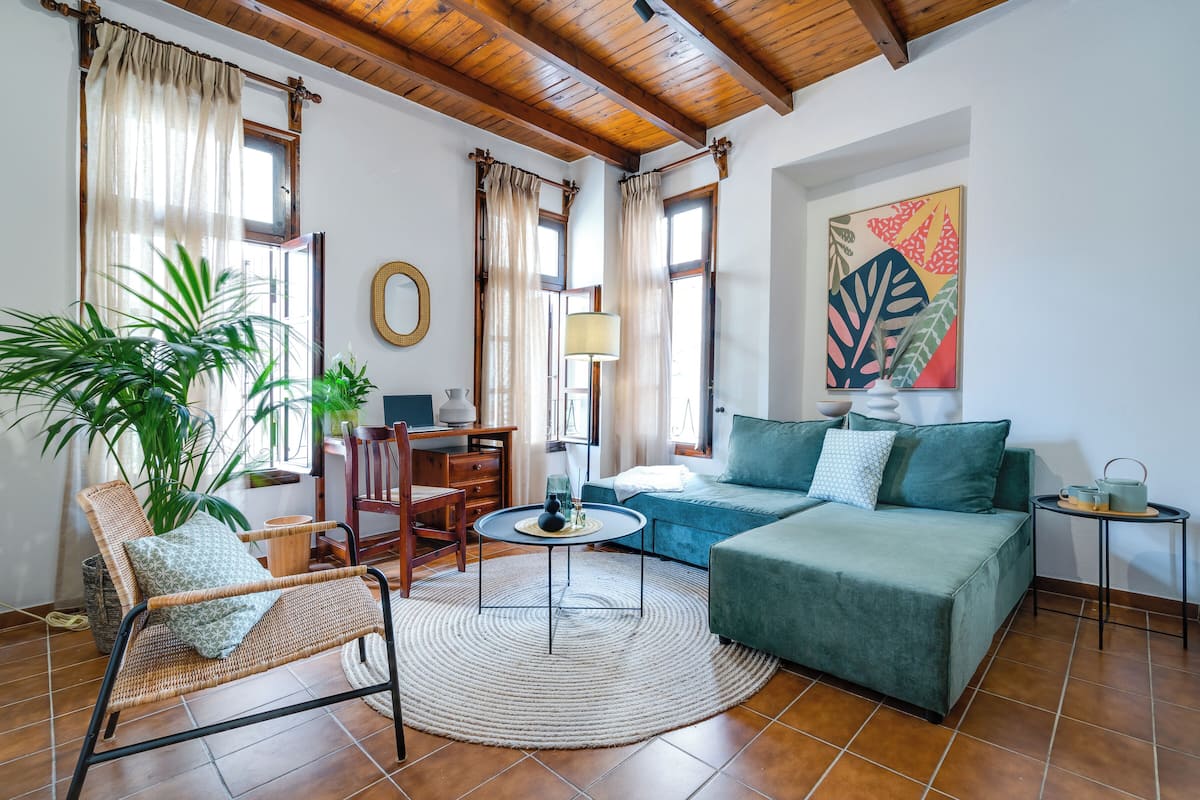 A cozy living room with a green sofa, a wicker chair, a round coffee table, and a large potted plant.