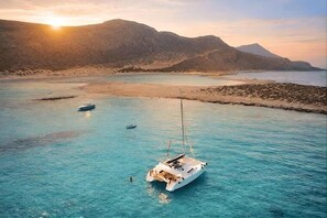 A white sailboat anchored in clear turquoise waters with a mountainous backdrop. - Monk Rooms (Chania)
