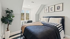 A bedroom with a bed, a potted plant, and a window.