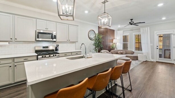 A modern kitchen with white cabinets, a central island with bar stools, stainless steel appliances, and pendant lighting.