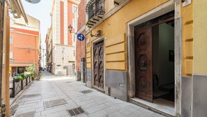 A narrow street with a building featuring a large wooden door and a blue directional sign. - Domu Arké by Propertize - above the ruins (Cagliari)
