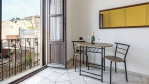 A balcony with a view of buildings, a wooden door, a small table with chairs, and a mirror on the wall. - Domu Arké by Propertize - above the ruins (Cagliari)