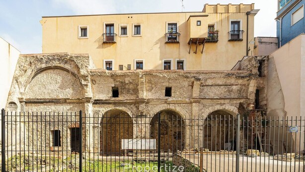 A historic building with arched doorways and a modern upper floor. - Domu Arké by Propertize - above the ruins (Cagliari)