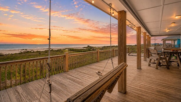 A wooden deck with a view of the beach and ocean at sunset.