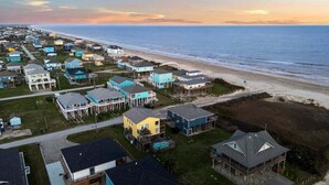 A coastal residential area with houses along the beach, a clear sky, and a sunset.