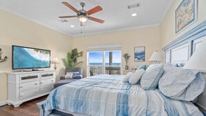 A bedroom with a bed, a television, a ceiling fan, and a window with a view.
