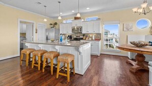 A spacious kitchen with white cabinetry, a central island with stools, a dining table with a bowl, and pendant lighting.