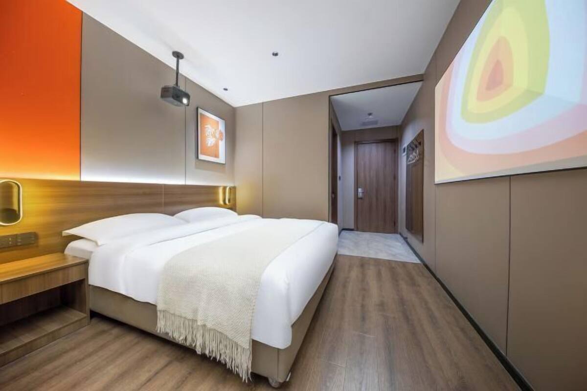 Une chambre d’hôtel moderne, dotée d’un grand lit, d’une table de chevet, d’un projecteur fixé au mur et d’une porte donnant sur une autre pièce.
