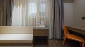 Une chambre d’hôtel avec un canapé, une petite table avec une lampe, une chaise et une fenêtre avec des rideaux.