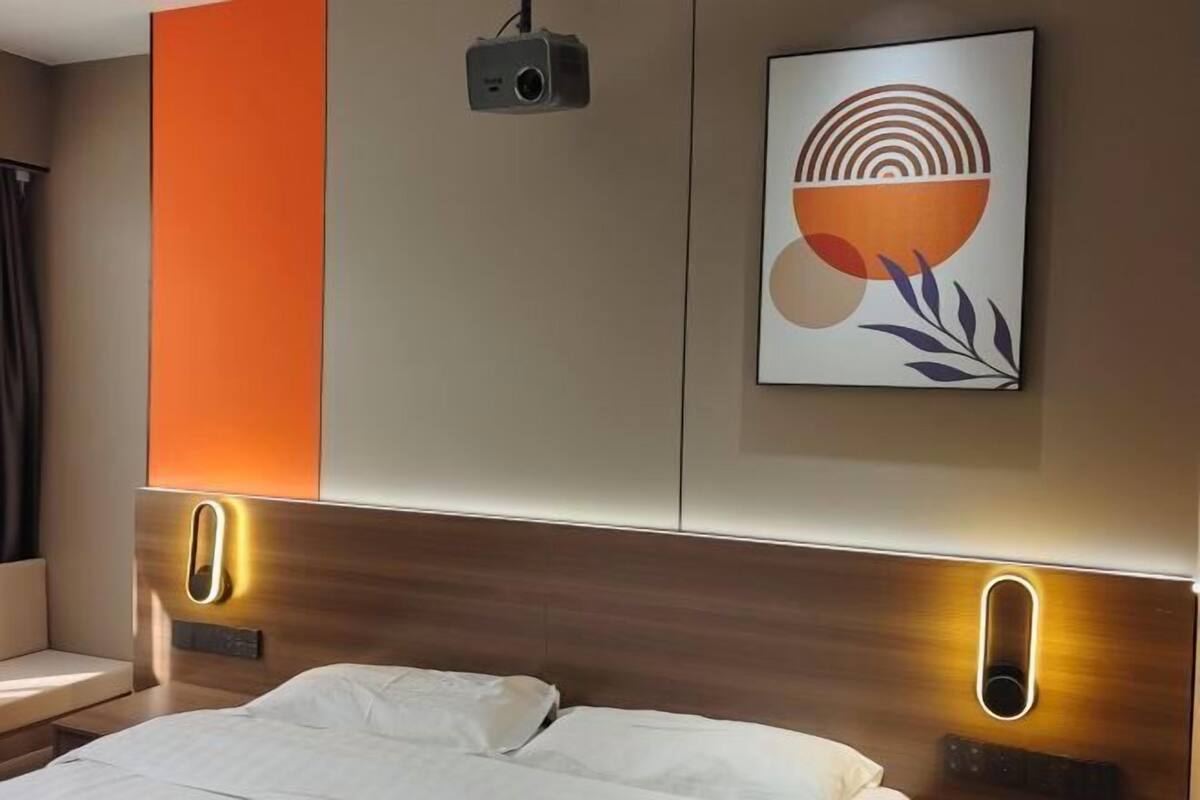 Une chambre d’hôtel moderne équipée d’un lit, d’un projecteur et d’une œuvre d’art accrochée au mur.