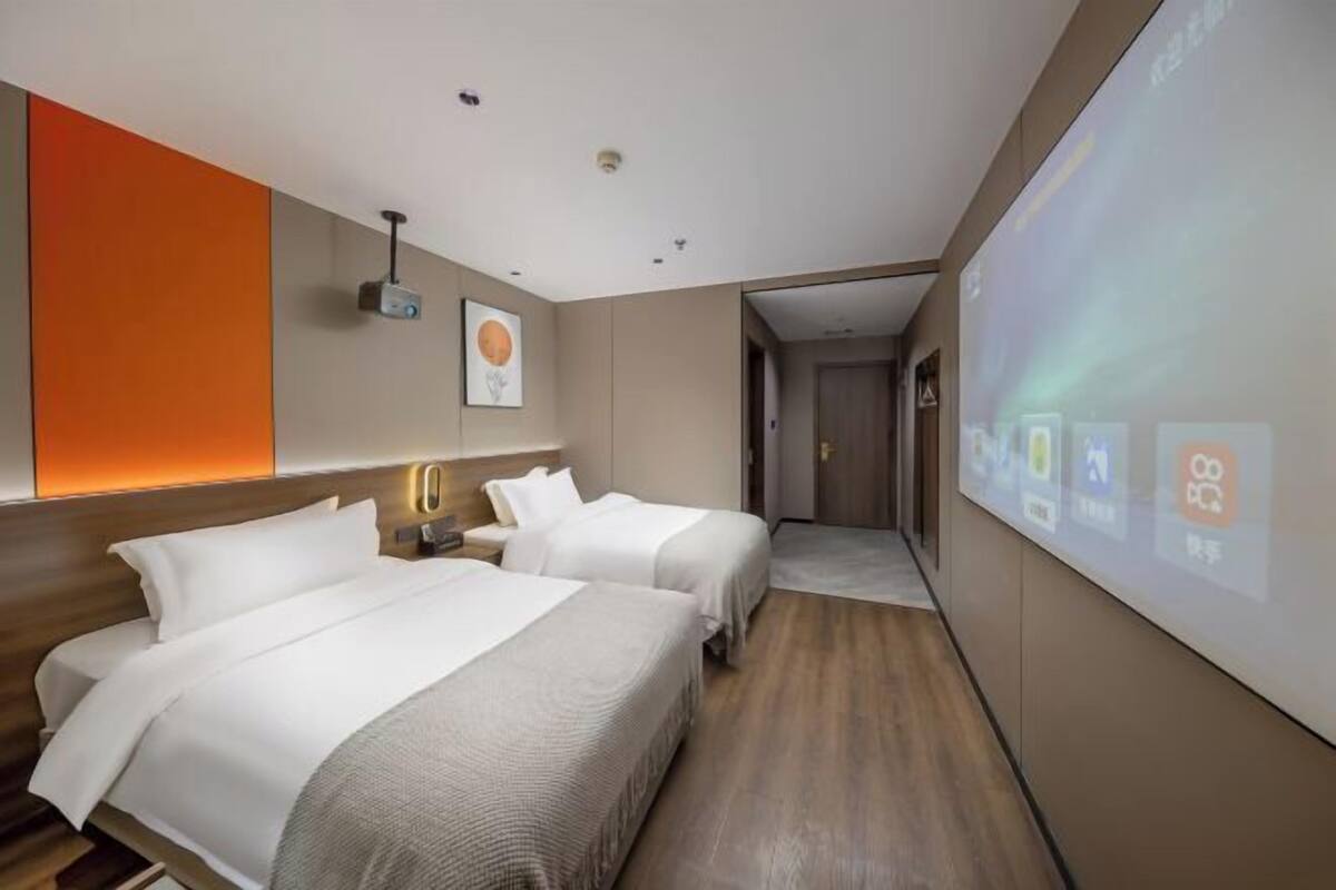 Une chambre d’hôtel avec deux lits, un écran de projection et un panneau de commande fixé au mur.