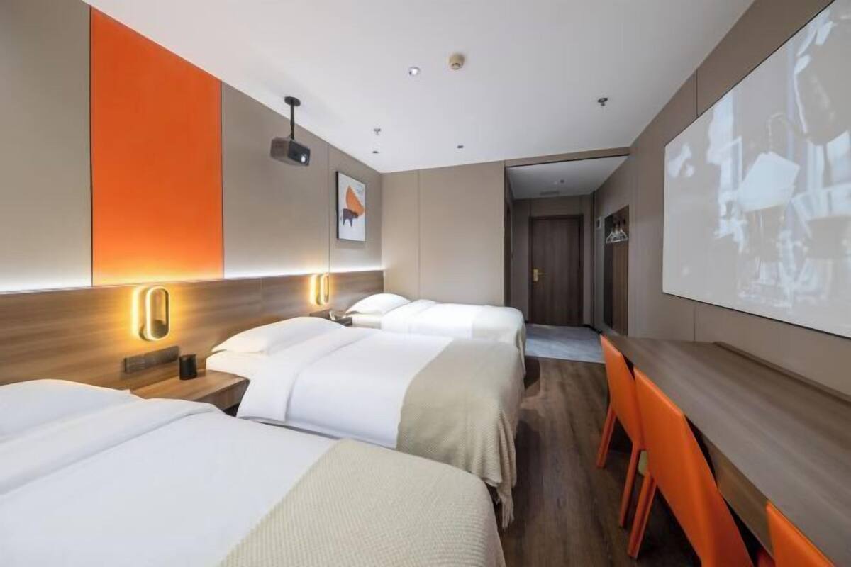 Une chambre d’hôtel avec deux lits, un bureau et un écran de projection.