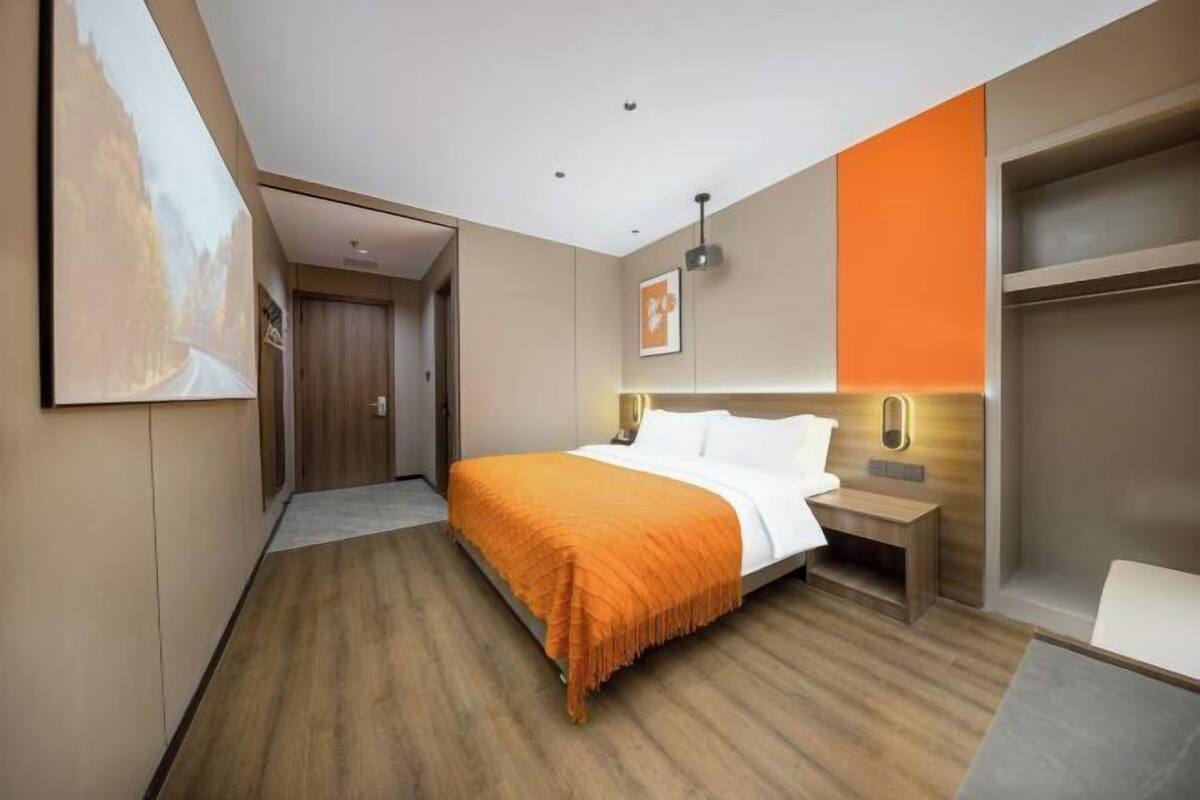 Une chambre d’hôtel moderne avec un grand lit, une table de chevet, une lampe fixée au mur et une armoire avec un miroir.