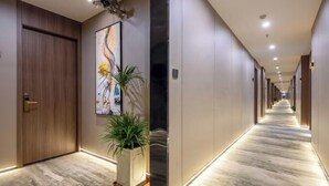 Ein langer, gut beleuchteter Korridor mit Marmorboden, Holztüren und einem großen abstrakten Gemälde an der linken Wand.