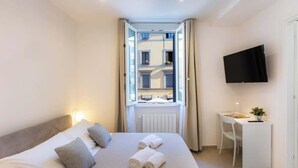 Una habitación de hotel con cama, escritorio, silla, televisión y ventana con cortinas.