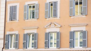 Fachada de edificio con múltiples ventanas, contraventanas y un elemento decorativo central.