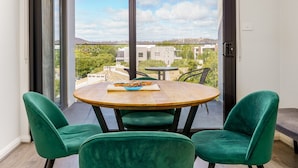 Een balkon met een ronde houten tafel en twee groene stoelen, met uitzicht op een stadsgezicht.