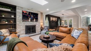 A modern living room with a stone fireplace, leather sofas, a flat-screen TV, and a dining area with a view of the outdoors.
