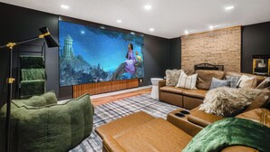 A modern living room with a large flat-screen TV, leather sofas, a green armchair, and a brick accent wall.
