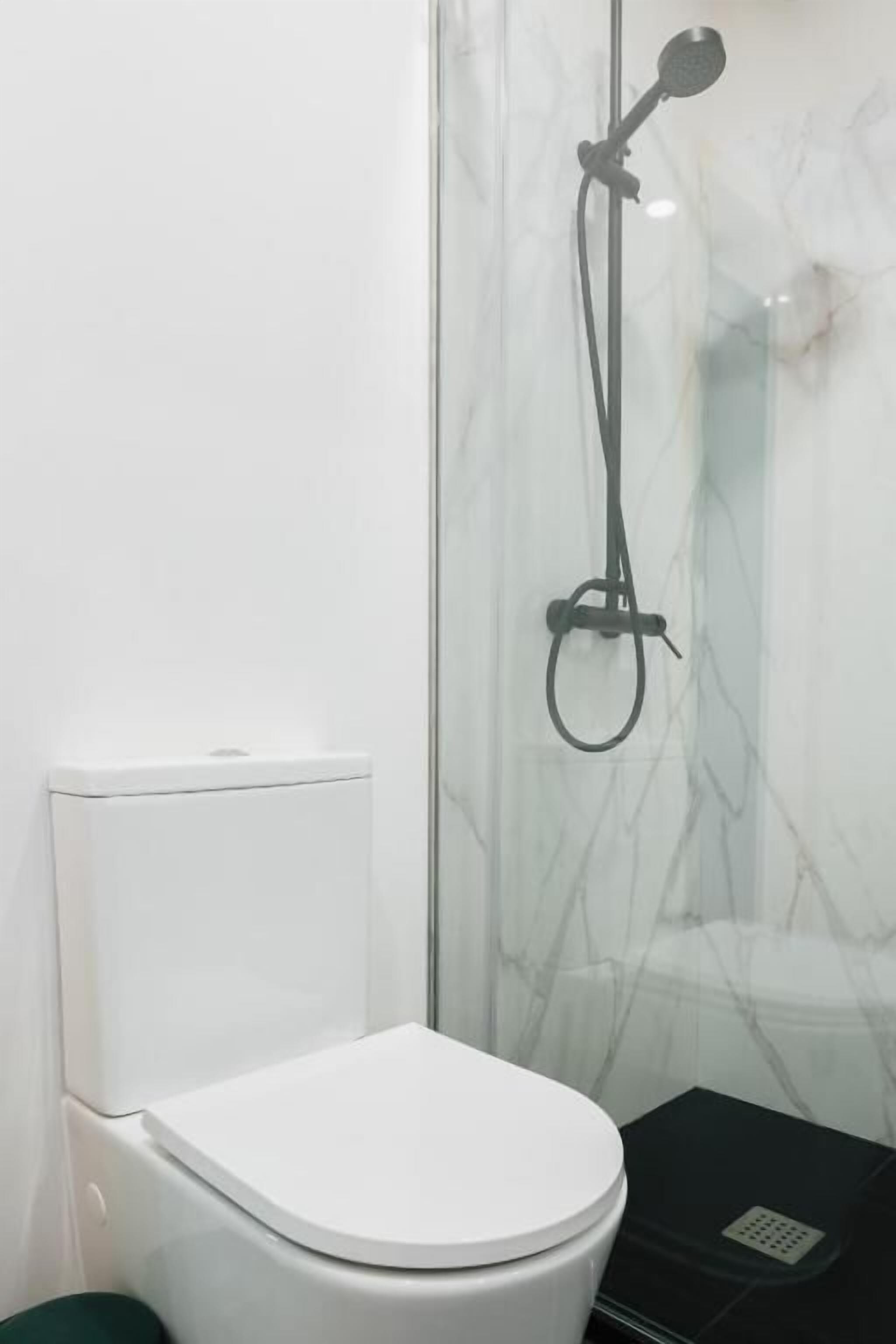 Un baño con inodoro blanco, cabina de ducha de cristal y un mueble de almacenamiento negro.