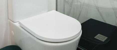 Un baño con inodoro blanco, cabina de ducha de cristal y un mueble de almacenamiento negro.