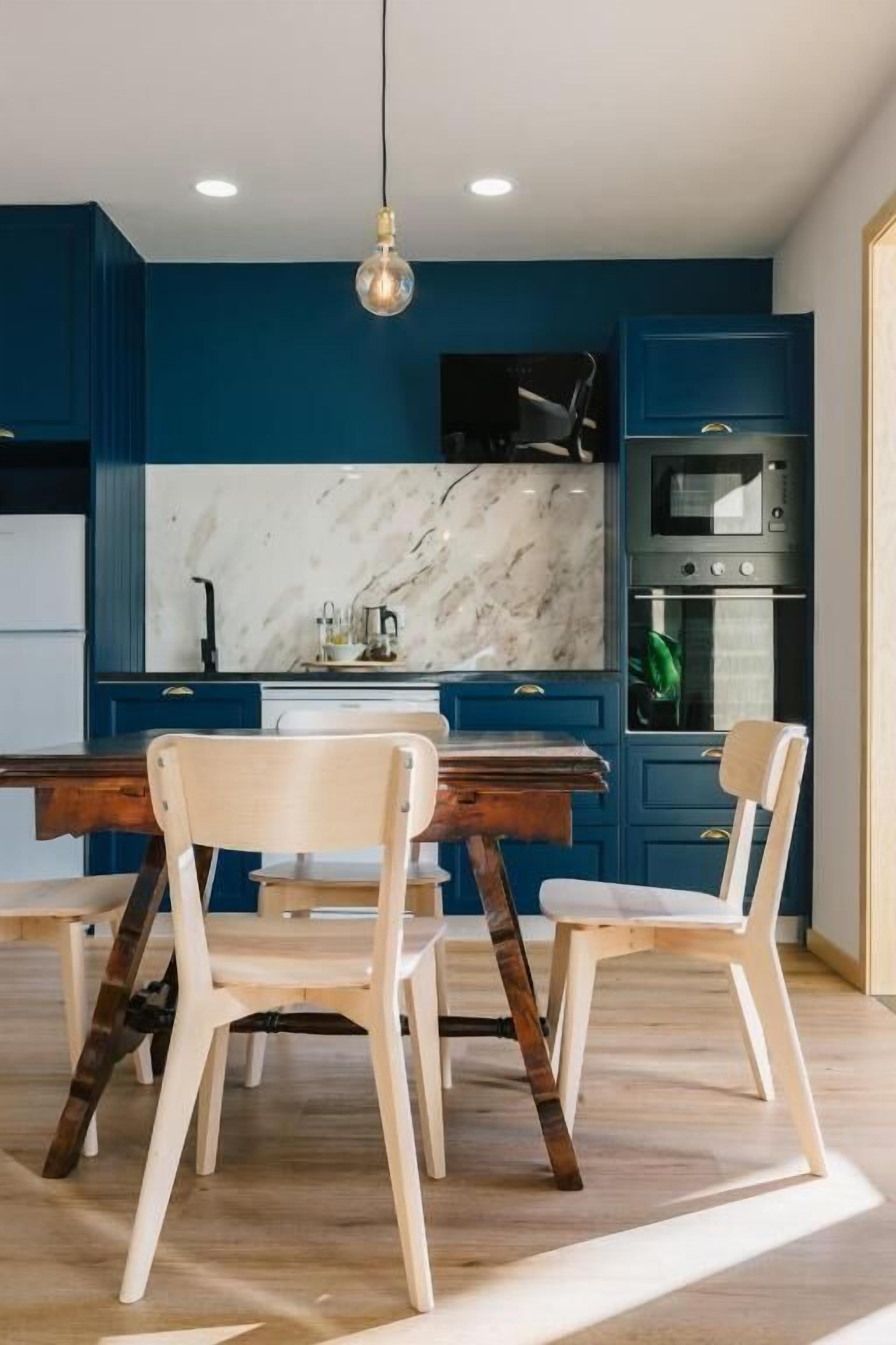 Une cuisine moderne avec des meubles bleus, un plan de travail en marbre et une table à manger en bois avec des chaises.