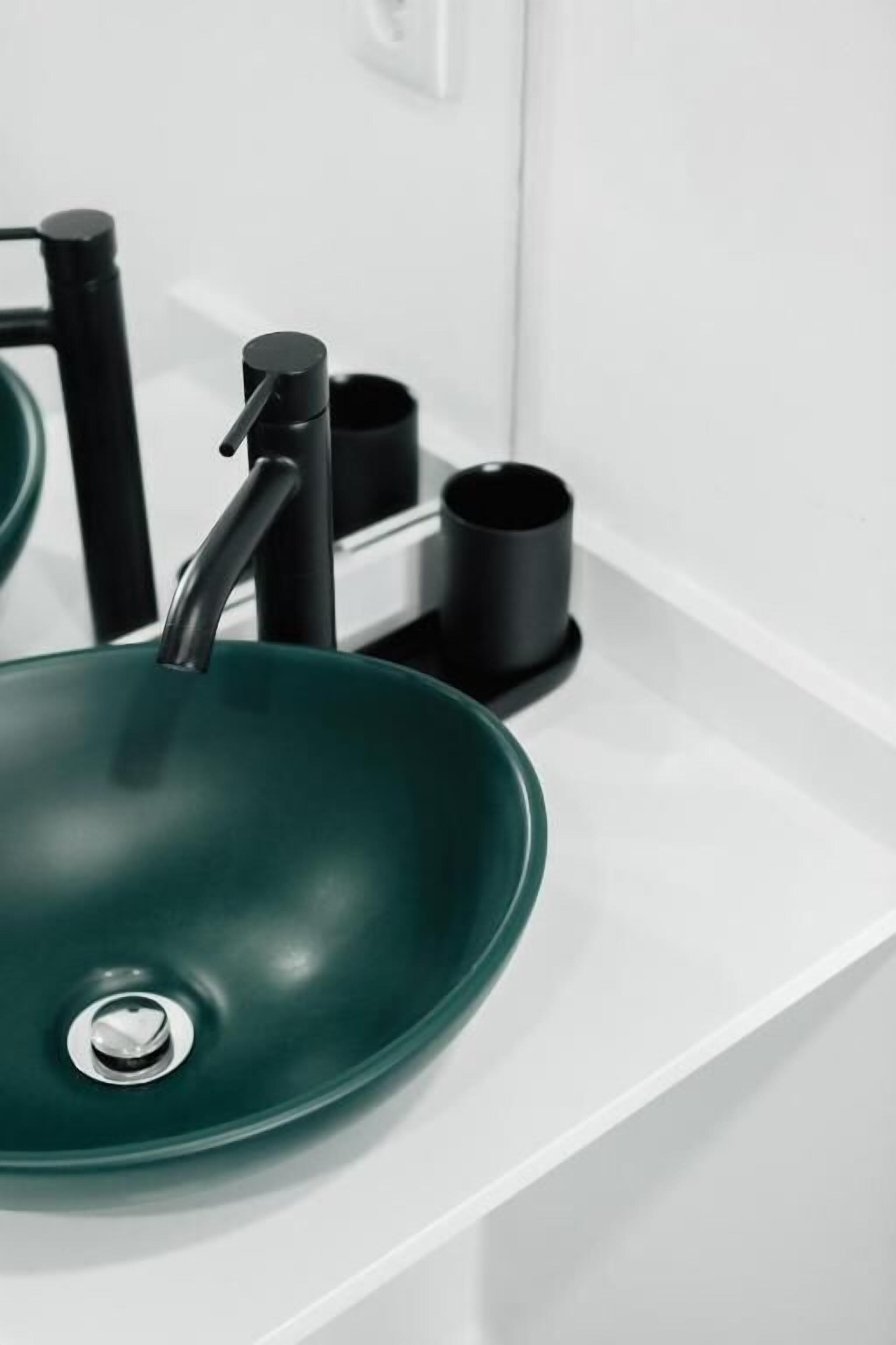 A modern bathroom with a green sink, black faucet, and black cup holder.