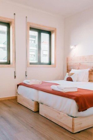 Un dormitorio con dos camas, cabecero de madera y ventana con vistas a edificios.