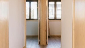 A narrow hallway with wooden flooring and white walls, leading to a room with a window and a radiator. - Campanha Apartment by Porto Stories (Porto)