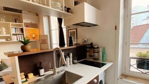 Una cocina compacta con un lavamanos integrado, armarios oscuros y repisas blancas.