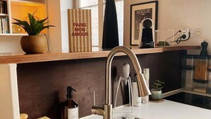 Una cocina moderna con un lavamanos de acero inoxidable, repisas de madera y una ventana con cortina negra.