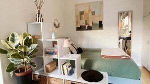 Un dormitorio moderno con una cama, una estantería blanca, una planta en maceta y un cuadro en la pared.